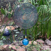 Decorative garden stake with a blue glass ball and metal dish on a natural background